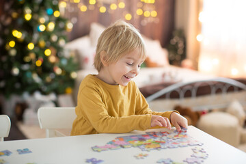Blond child, toddler boy, having fun at home on Christmas,  assembling puzzle, enjoying