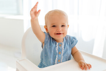Smiling little girl sitting on white feeding table. Portrait of cute and funny baby.