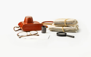 A stack of family photos and a film camera, glasses and a magnifier on a white background.