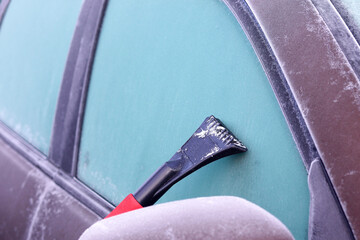 The frozen glass of the car is cleaned with a scraper