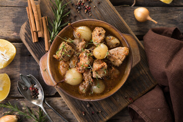 stifado - delicious mediterranean beef stew with onion bulbs, cinnamon and spices in a casserole, on a black wooden table, view from above, close-up