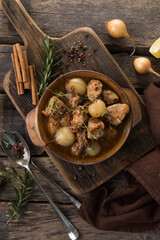 stifado - delicious mediterranean beef stew with onion bulbs, cinnamon and spices in a casserole, on a black wooden table, view from above, close-up