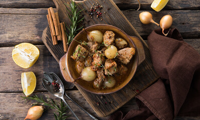 Stew. stifado - delicious mediterranean beef stew with onion bulbs, cinnamon and spices in a casserole, on a black wooden table, view from above, close-up