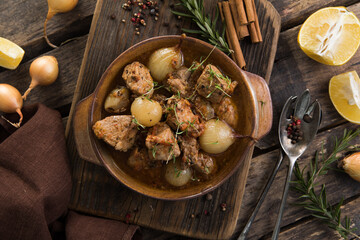 stifado - delicious mediterranean beef stew with onion bulbs, cinnamon and spices in a casserole, on a black wooden table, view from above, close-up