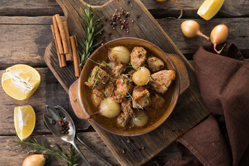 stifado - delicious mediterranean beef stew with onion bulbs, cinnamon and spices in a casserole, on a black wooden table, view from above, close-up