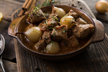 stifado - delicious mediterranean beef stew with onion bulbs, cinnamon and spices in a casserole, on a black wooden table, view from above, close-up