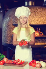 Little girl dressed as a cook with vegetables in her hands.