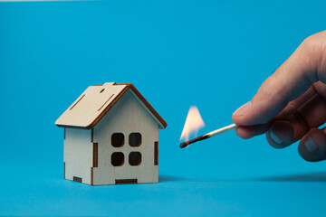 A burning match next to a wooden house on a blue background. Real estate insurance concept....