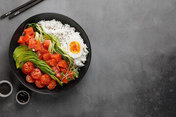 Poke bowl with salmon, avocado and rice on dark background with chopsticks. Top view