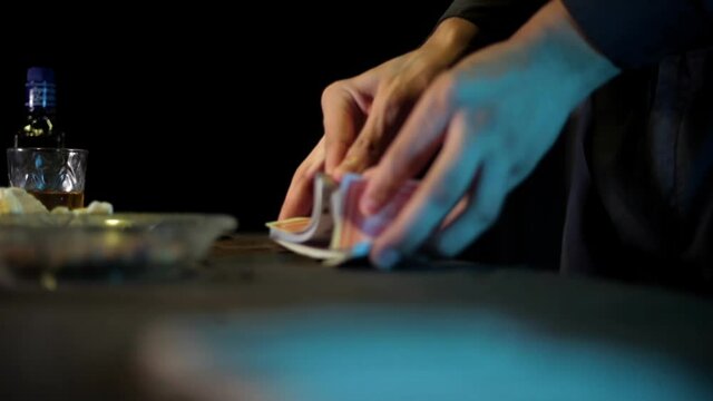 Close-up shot of a magician shuffling cards on the table in dark lighting, high-resolution footage.
