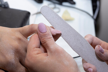 cropped image of nail technician filing nails to customer with nail file