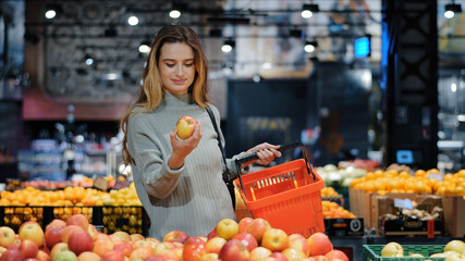 Young business woman girl buyer client blonde lady consumer stands in shop near counter with fruits...