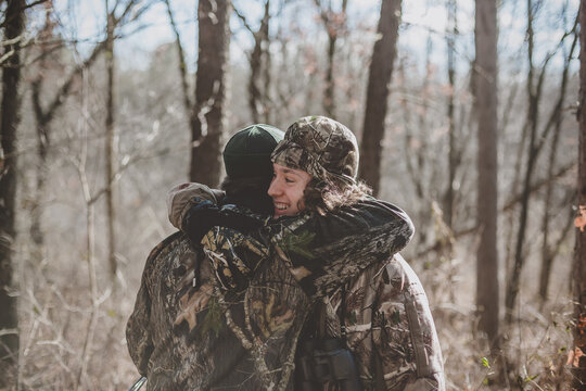 Father and son deer hunter's hugging in woods