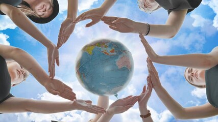 Schoolgirls hug the earth globe with their hands, making a circle out of them on the background of the magic sky.