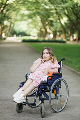 Fototapeta na wymiar Portrait of pleasant young woman with spinal muscular atrophy smiling on camera among green summer park. Female person who using wheelchair. Concept of people with disability.