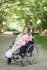Fototapeta na wymiar Portrait of pleasant young woman with spinal muscular atrophy smiling on camera among green summer park. Female person who using wheelchair. Concept of people with disability.