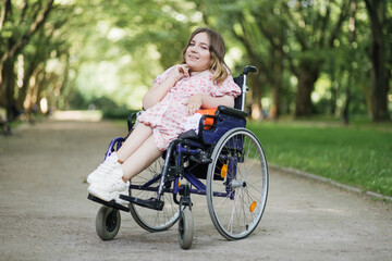 Portrait of pleasant young woman with spinal muscular atrophy smiling on camera among green summer...