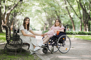 Fototapeta na wymiar Pretty woman with disability holding hands with her female friends that sitting on wooden bench among green park. Two females enjoying common walk during summer time.
