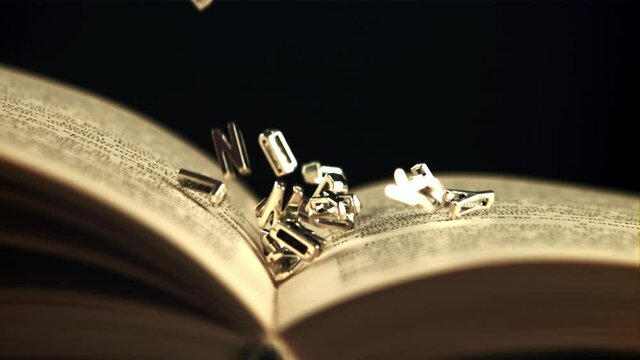 English letters fall on an open book. On a black background. Filmed is slow motion 1000 frames per second. High quality FullHD footage