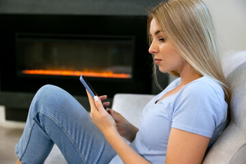Portrait of a beautiful woman using her smartphone in the living room while relaxing on the sofa.