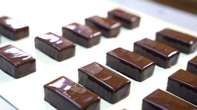 Chocolate candy bars of pigeon&rsquo;s milk. Shiny sweets move along the conveyor belt at the confectionery plant. Close up.