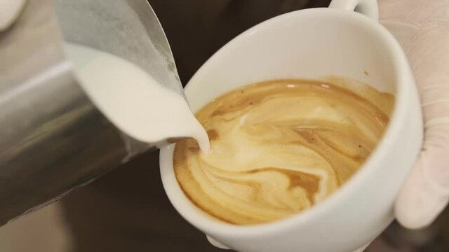 Close up barista hands pouring warm milk in coffee cup for making latte art.