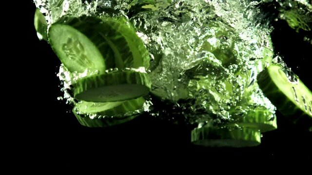 Pieces of fresh cucumber fall under the water with air bubbles. On a black background. Filmed is slow motion 1000 frames per second.