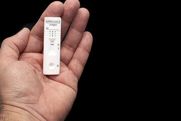 A man's hand holding the rapid sars-cov-2 antigen test card, on a black background.