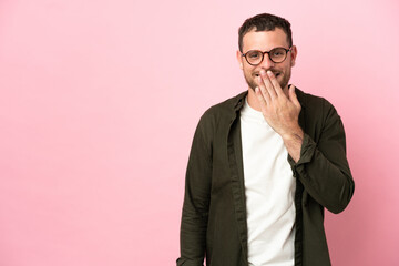 Young Brazilian man isolated on pink background happy and smiling covering mouth with hand