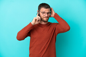 Young Brazilian man using mobile phone isolated on blue background having doubts