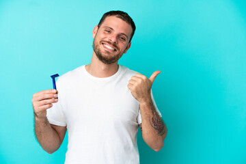 Brazilian man shaving his beard isolated on blue background pointing to the side to present a product