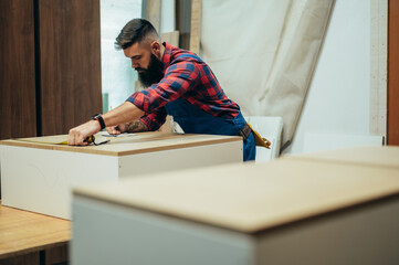 Young male carpenter working in workshop and measuring with meter