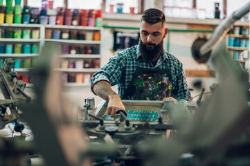 Male worker using printing machine in a workshop