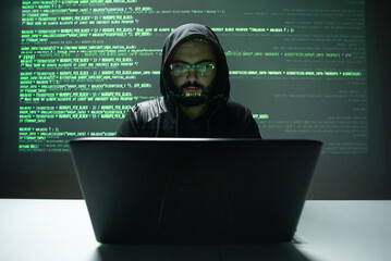 Hispanic man in front of his laptop with green coding  behind him on a screen