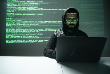 Hispanic man in front of his laptop with green coding  behind him on a screen