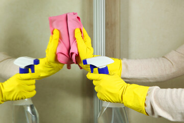 Woman in gloves wipes the mirror with detergents close-up