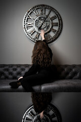 Girl and time. Beautiful young girl posing against the background of a wall clock - obrazy, fototapety, plakaty
