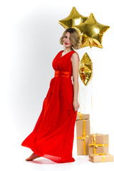 Party photo of elegance sexy lady in red dress with red lips and blond beautiful curly hair, smiling. Background of gold air balloons and gifts. Concept of the sale