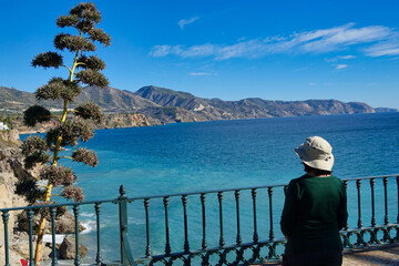 Woman with a hat on her back looking at the Mediterranean Sea and the Costa del Sol from the Punta de Europa viewpoint in Nerja (Spain)
