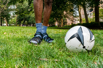 Soccer ball and mans legs on lawn in park