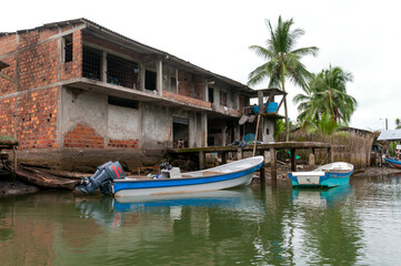 Fototapeta na wymiar Outboard motor boat in front of a red brick house in a fishing village on the Colombian Pacific coast.