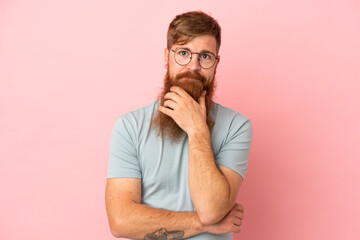 Young reddish caucasian man isolated on pink background thinking