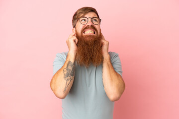 Young reddish caucasian man isolated on pink background frustrated and covering ears