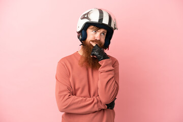 Young reddish caucasian man with a motorcycle helmet isolated on pink background having doubts and thinking