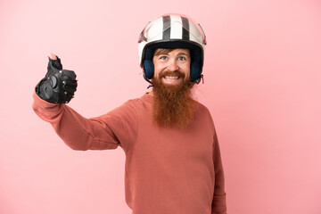 Young reddish caucasian man with a motorcycle helmet isolated on pink background with thumbs up because something good has happened