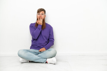 Young caucasian reddish man sitting on the floor isolated on white background surprised and shocked while looking right
