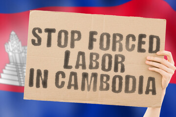 The phrase " Stop forced labor.in Cambodia " on a banner in men's hand with blurred Cambodian flag on the background. Illegal. Horrible. Stressful. Dangerous. Community. Worker. Violence. Right