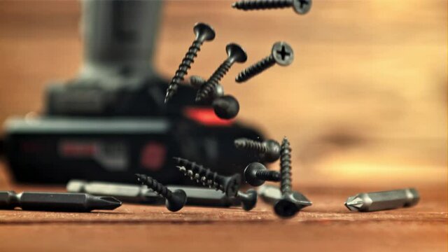 Self-tapping screws fall on a wooden table. On a wooden background. Filmed is slow motion 1000 frames per second.