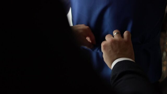 An HD video of an unrecognizable man tying the belt around the groom's suit