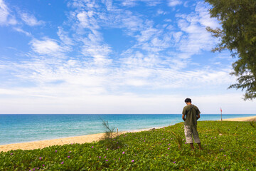 a man stand on morning glory beside the beach flying a drone..scenery white cloud in blue sky green sea in Andaman ocean..travel of nature and technology concept.